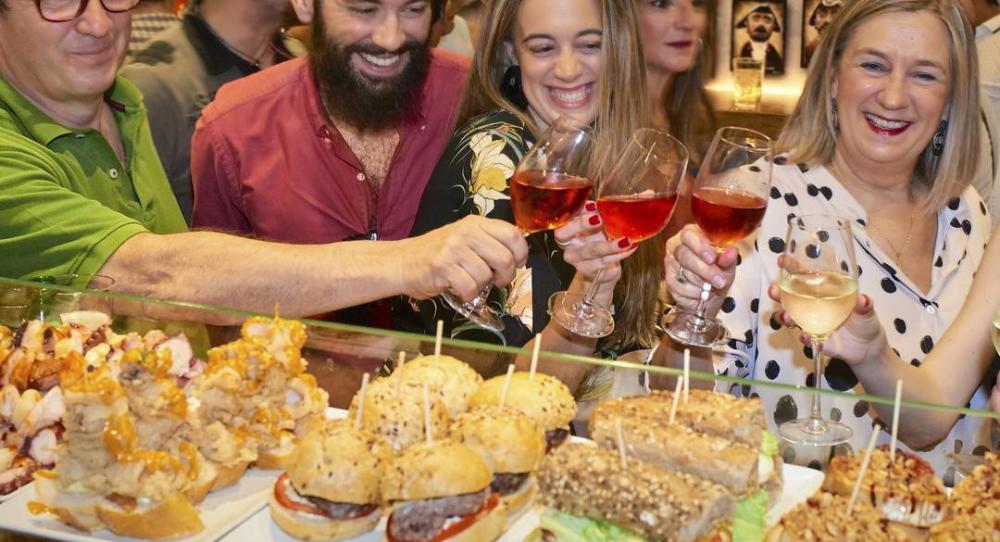 Amigos y amigas brindando junto a una barra repleta de pinchos